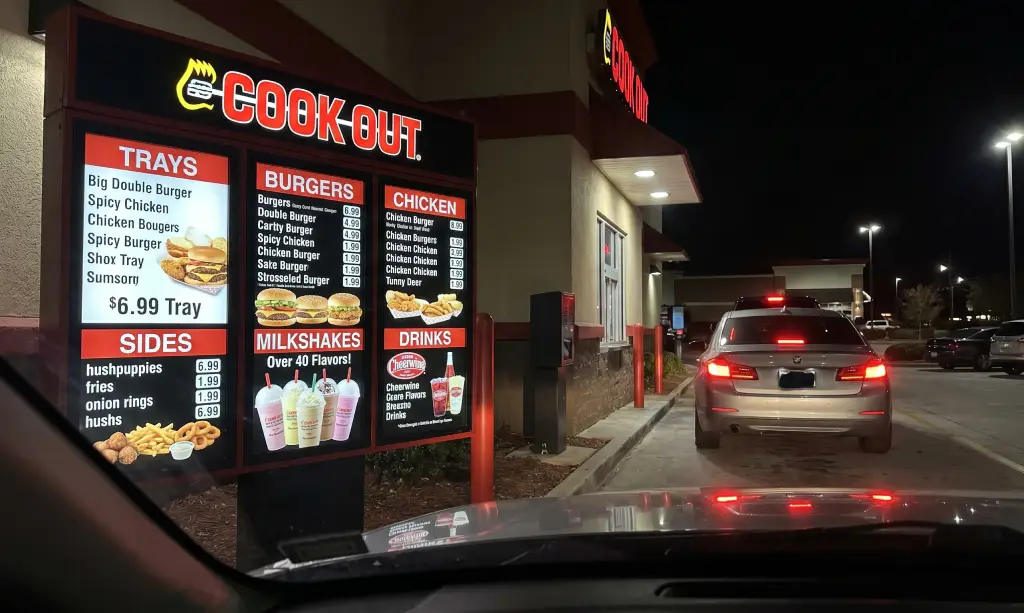 Cook Out restaurant drive-thru with illuminated menu board showing Cook Out Menu Prices